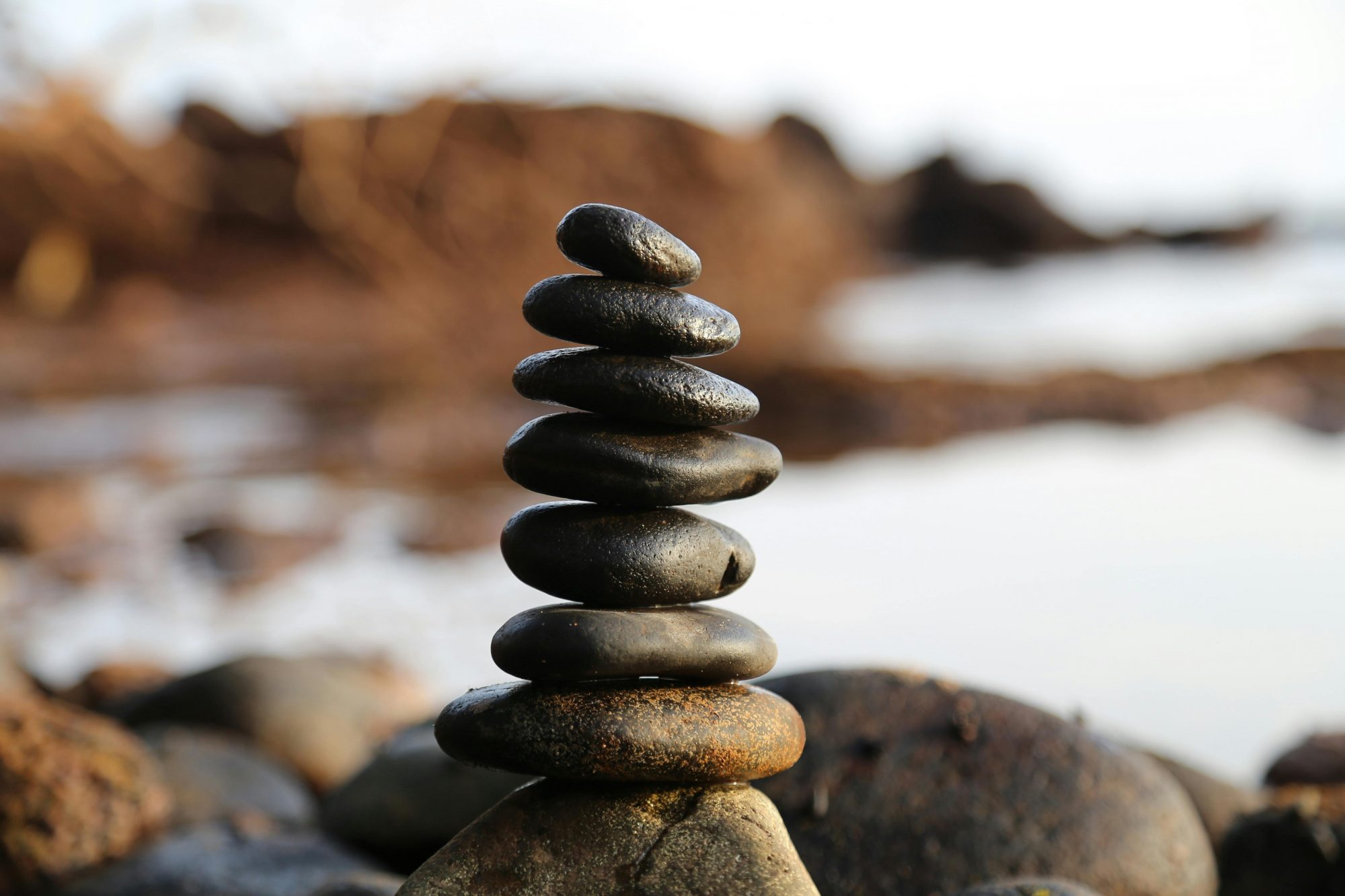 Stacked black stones balanced on a rocky shoreline, symbolizing stability, discipline, and thoughtful investment in AI