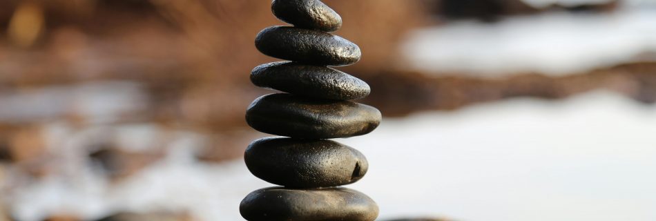 Stacked black stones balanced on a rocky shoreline, symbolizing stability, discipline, and thoughtful investment in AI